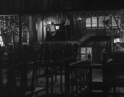 Image of two men on the stage in a darkened, closed tavern, while a third man watches from the barle 