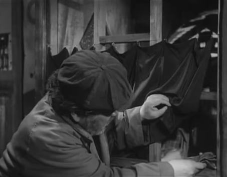 A man with a cap passes some money to an unseen woman across the bar, under a small curtain