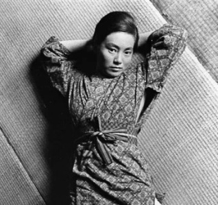 Photo of a young modern Japanese woman in a kimono, lying on the floor and staring up at the camera in a provocative pose