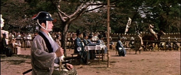 In ancient Japan, a number of judges review a tournament, while a mounted rider appears in the background