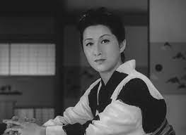 A middle-aged woman in traditional Japanese kimono, seated and staring into the camera