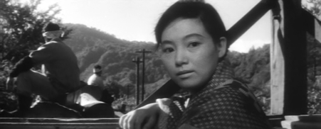 On a train traveling through the hills of northern Japan, a young Japanese woman looks back in the direction of the camera and seems interested in what she sees