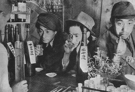 Black-and-white photo of several Japanese men of indeterminate age, sitting at a bar surrounded by bottles of alcohol. 