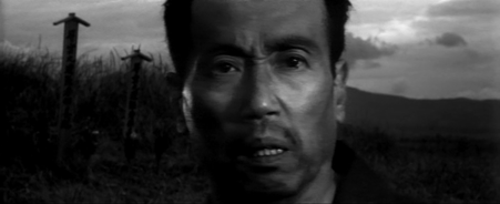 Close-up of a middle-aged Japanese man's face with a look of amazement, against a background of fields and mountains amid the setting sun