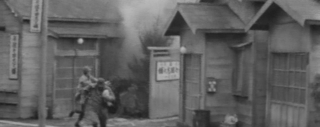 Two Japanese men in military uniforms are indistinctly seen running from a building on fire