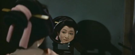 An attractive young woman in the clothing of feudal Japan examines her face in the mirror