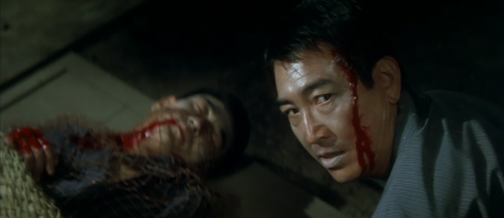 A color photo of the Japanese man, with blood on his face, looking behind him at something, while the dead Japanese lies on the ground