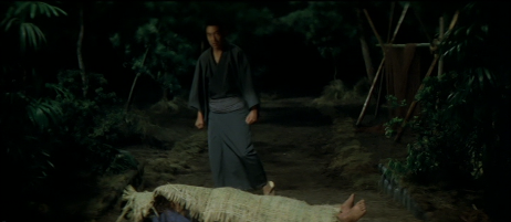 At night, a Japanese man wearing kimono approaches a man lying on the ground, covered by a bamboo "shroud"