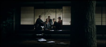 Four Japanese in traditional dress, three men and a woman, are seated in the doorway of a house, looking at a tree in the front yard; an older man in the group, grinning, holds a pistol