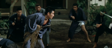 In a yard, a Japanese  man in traditional clothing, obviously weakened and caught in a kind of rope net, faces a gang of armed swordsman who surround him