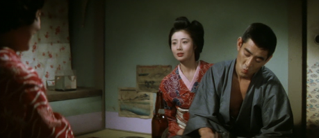 A Japanese woman in traditional clothing, sitting on the floor, listens distraught to another woman (with her back to the camera), while a Japanese man, in kimono, sits nearby