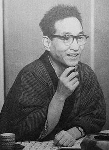 A snapshot of a Japanese man in his 40s wearing kimono and glasses and with a cigarette in his hand