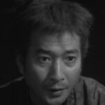 Picture of a surprised-looking Japanese man, shown against a dark (night) background, wearing clothing from Japan's feudal era