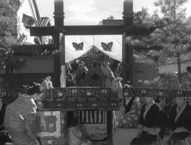 A crowded daytime scene as a little girl is seated in a palanquin that's about to be closed, as retainers and serving maids kneel quietly waiting to resume their journey to Edo