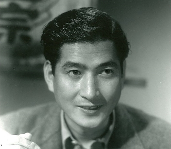 Headshot of a Japanese man of about 35, wearing modern clothes, smiling at something to one side of the camera