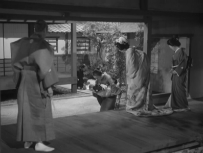 The traditionally-dressed Japanese woman, Shigenoi, talks to an old woman  who is holding a baby and standing in a courtyard on a slightly lower level, while two elderly people, her parents, stand and watch the scene