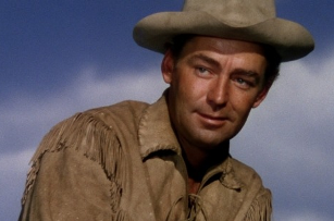 A young man wearing the costume of a Western cowboy smiles at something off-camera