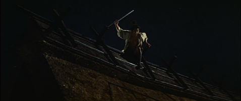 A young Japanese man in samurai dress stands at night on a rooftop, his sword drawn, shouting at someone below