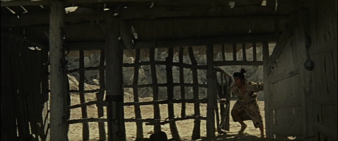 A young Japanese man in feudal costume enters a deserted hut in the middle of a wasteland