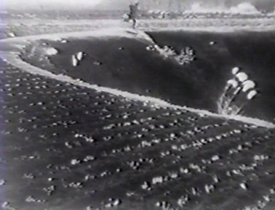 A shot of a field at night showing (top center) a man in the far distance running