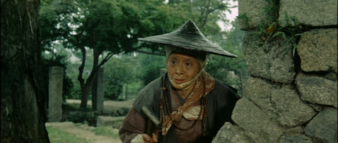 An old Japanese woman in feudal costume and a sedge hat, looking at something in the general direction of the camera, with tears in her eyes