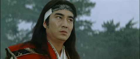 A young Japanese man in period costume and wearing a headband, in a rural area in the morning, looks anxiously towards something off-camera