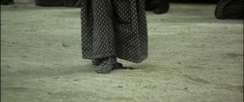 A shot of a man in feudal costume from the knees downward, with his feet resting on sand